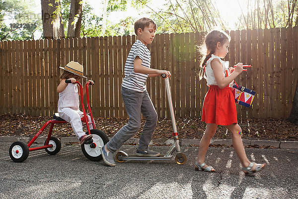 Drei Kinder in Mini-Parade,  Trommelschlagen,  Dreiradfahren und Rollerfahren