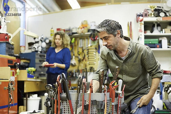 Reife männliche Freiwillige,  die mit Werkzeugen gegen weibliche Kollegen in der Werkstatt arbeiten.