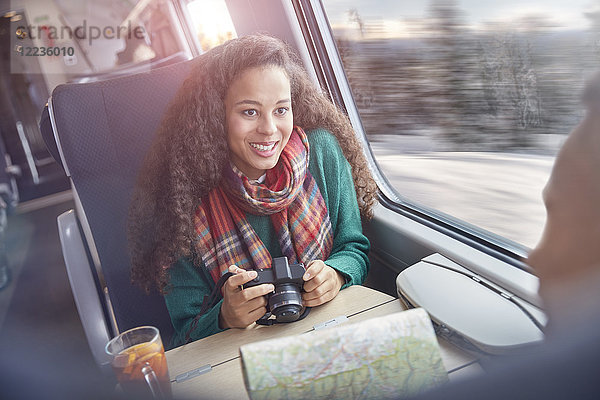 Lächelnde junge Frau mit Kamera und Karte im Personenzug