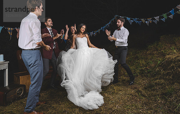 Fröhliche Braut beim Tanzen und Spaß haben,  während ihre Freunde auf einer Nachtfeld-Party klatschen.