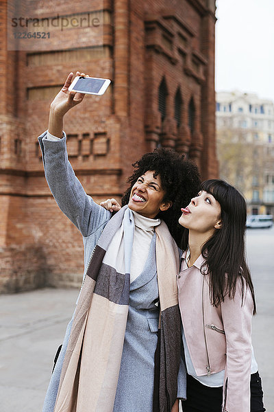 Spanien,  Barcelona,  zwei verspielte Frauen,  die einen Selfie an einem Tor nehmen.