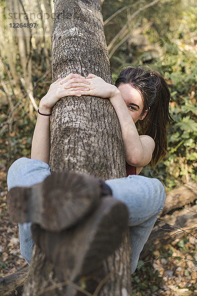 Fröhliche junge Frau umklammert einen Baumstamm