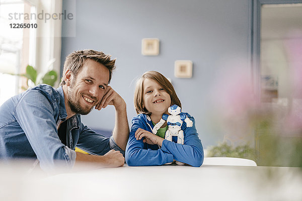 Porträt eines glücklichen Vaters und Sohnes mit Roboter zu Hause