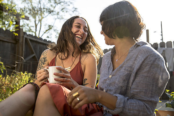 Zwei glückliche junge Frauen,  die im Hinterhof reden.