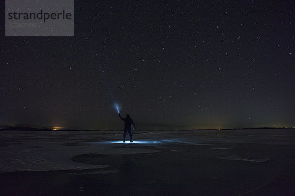 Russland,  Oblast Amur,  Silhouette des Menschen mit blauem Strahl auf dem gefrorenen Fluss Zeya bei Nacht unter dem Sternenhimmel.