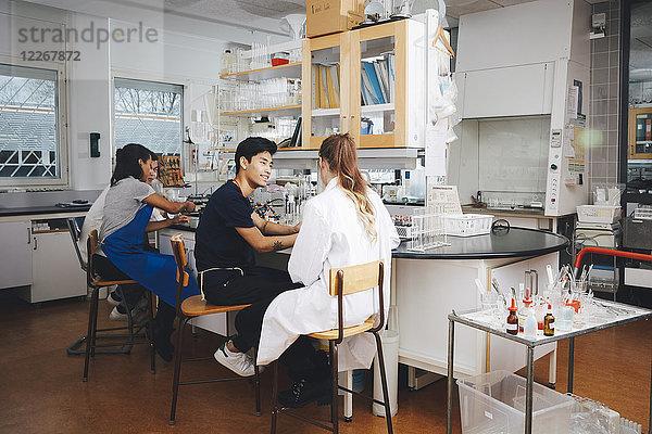 Multi-ethnische junge Universitätsstudenten sitzen auf Lehrstühlen im Chemielabor