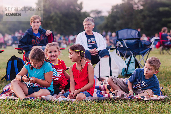 Gruppe von Erwachsenen und Kindern,  im Freien sitzend,  während der Feierlichkeiten zum 4. Juli
