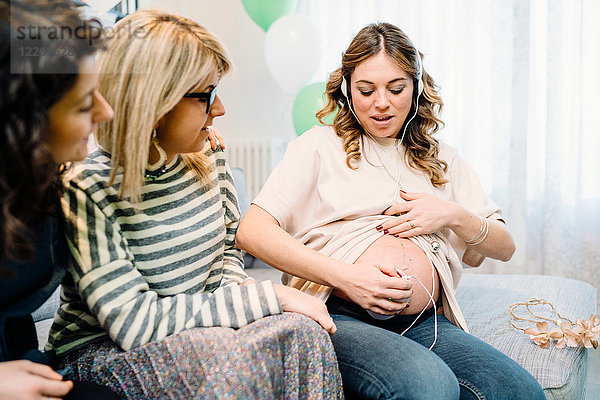 Schwangere und Freundinnen auf dem Sofa mit pränatalem Hörgerät