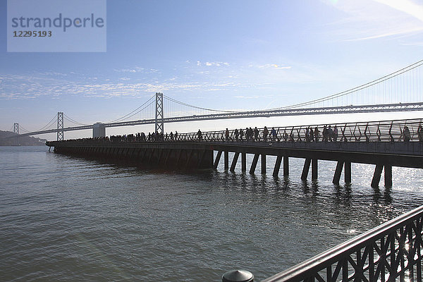 Menschen am Pier mit Oakland Bay Bridge über der Bucht im Hintergrund,  San Francisco,  USA
