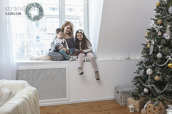 Frau sitzend mit Kindern auf der Fensterbank zu Hause zu Weihnachten