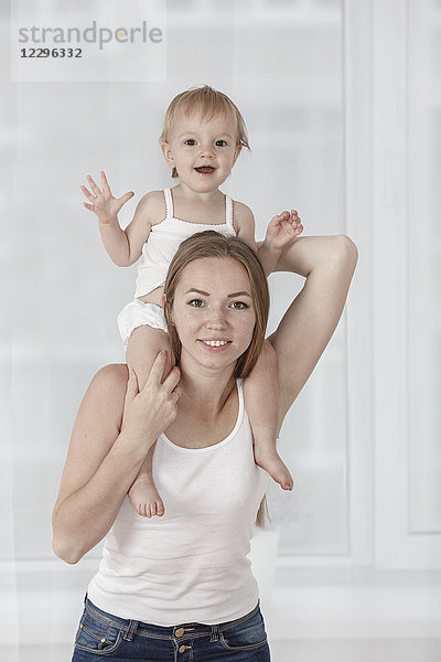 Porträt einer glücklichen Mutter,  die ihre Tochter auf den Schultern trägt.