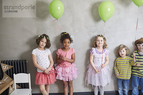 Porträt von Mädchen und Jungen mit grünen Luftballons,  die an der Wand stehen