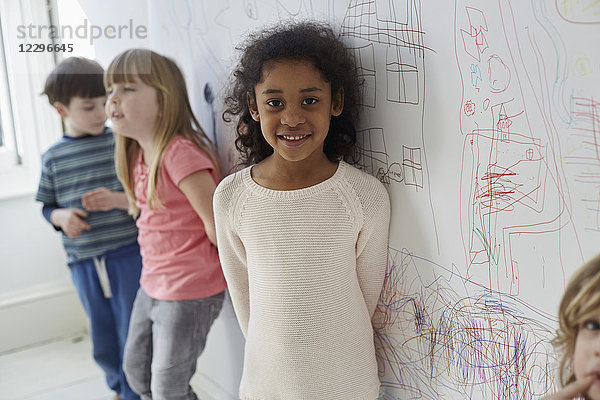 Porträt eines Mädchens,  das mit Freunden gegen Zeichnungen an der Wand steht.