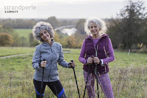 Portrait confident active senior women hikers with poles in rural field