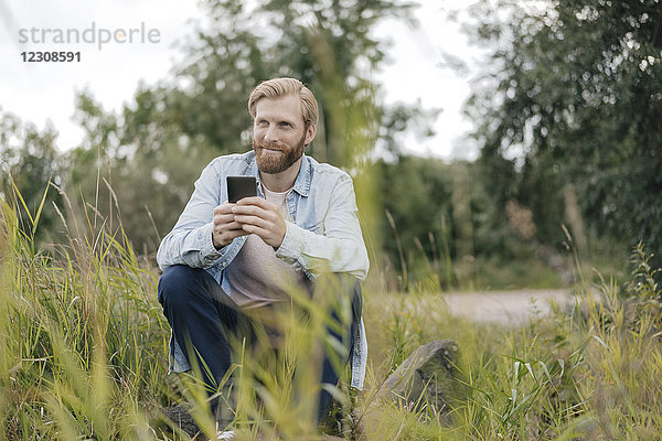 Lächelnder Mann mit Smartphone in der Natur