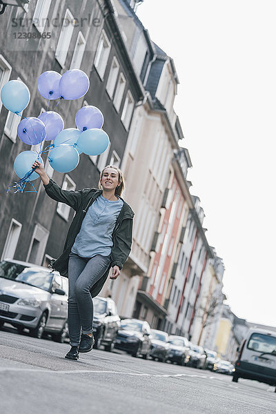 Glückliche Frau mit blauen Luftballons auf der Straße