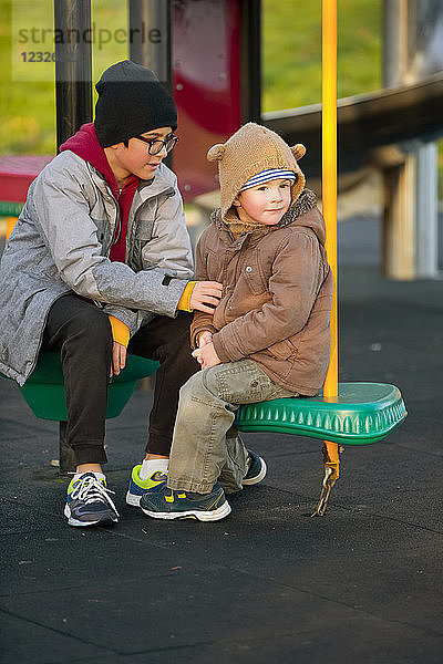 Ein kleiner Junge und sein älterer Bruder sitzen und unterhalten sich auf einem Spielplatz; Langley,  British Columbia,  Kanada