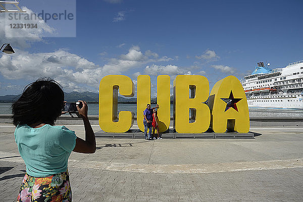 Kuba,  Santiago de Cuba,  eine kubanische Familie fotografiert sich vor einem großen Denkmal in Form des Wortes CUBA am Hafen von Santiago