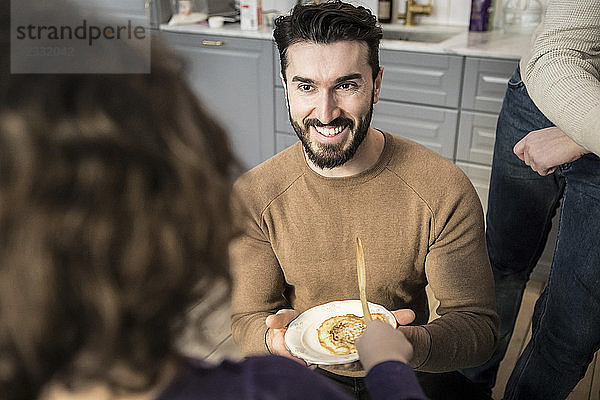Smiling young father offering pancake to daughter in kitchen