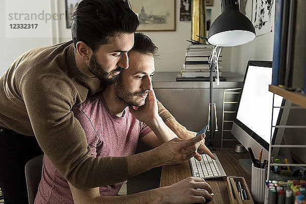 Gay couple looking at credit card while shopping online on computer at home