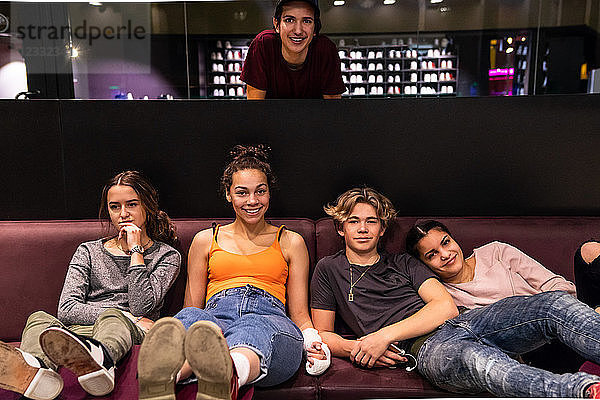 Portrait of multi-ethnic teenage friends on sofa at bowling alley