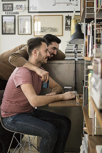 Side view of gay couple shopping online through computer at home
