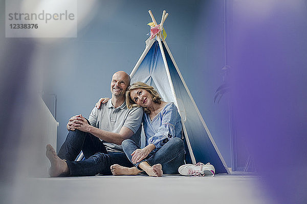 Smiling couple sitting at teepee indoors