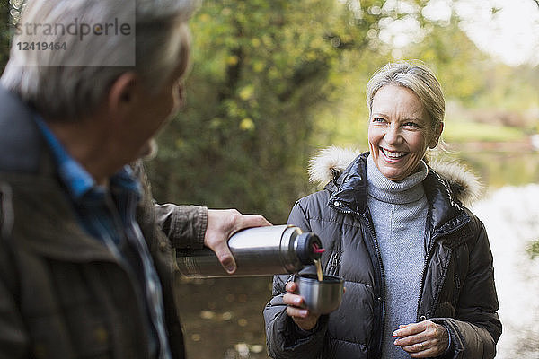 Glückliches reifes Paar trinkt Kaffee aus einem isolierten Getränkebehälter im Herbstpark
