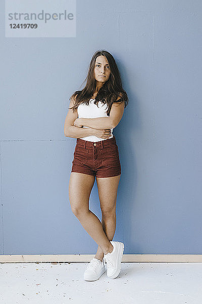Young woman leaning against wall with arms crossed