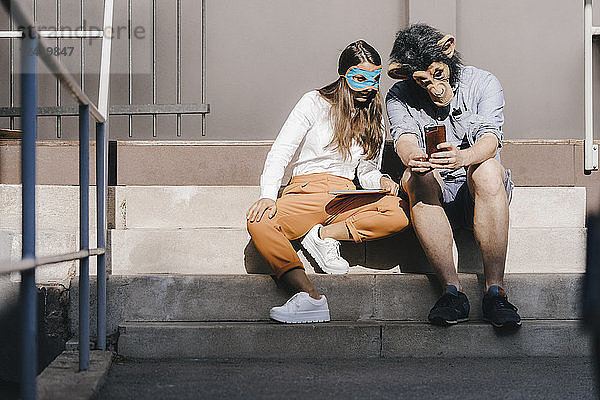 Couple in disguise sitting on stairs,  using smartphone