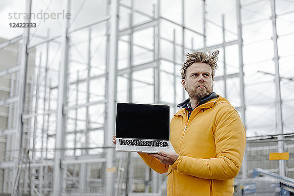 Man holding laptop,  construction site in the background