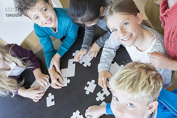 Portrait of smiling pupils playing jigsaw puzzle in school together