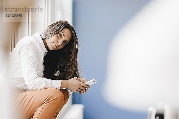 Young businesswoman sitting at window,  using smartphone