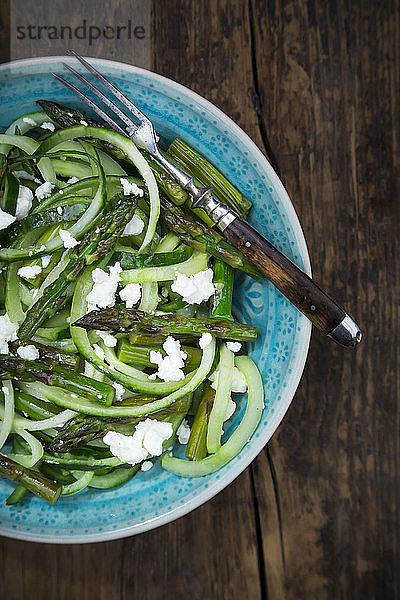 Bowl of green asparagus salad with helically coiled cucumber and feta cheese