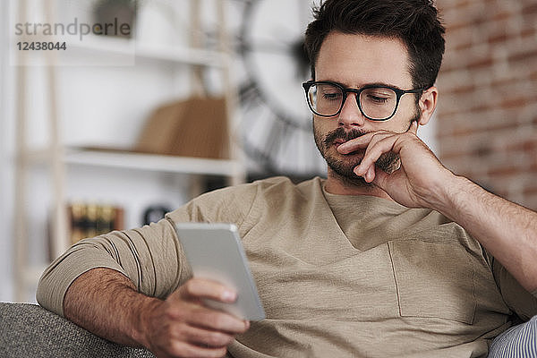 Portrait of man sitting on couch at home looking at smartphone