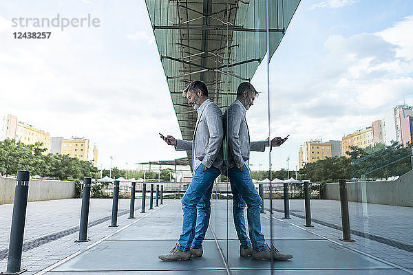 Businessman leaning against glass facade using smartphone