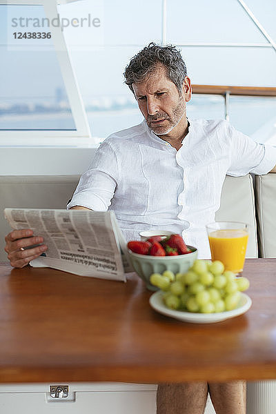 Mature man on a sailing trip having a healthy breakfast,  reading newspaper