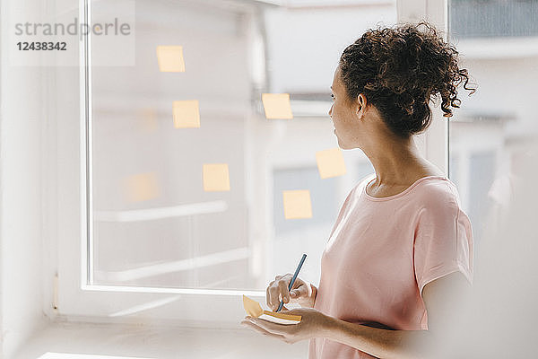 Woman posting adhesive notes on window,  brainstorming