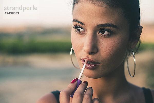 Portrait of teenage girl in nature applying lip gloss