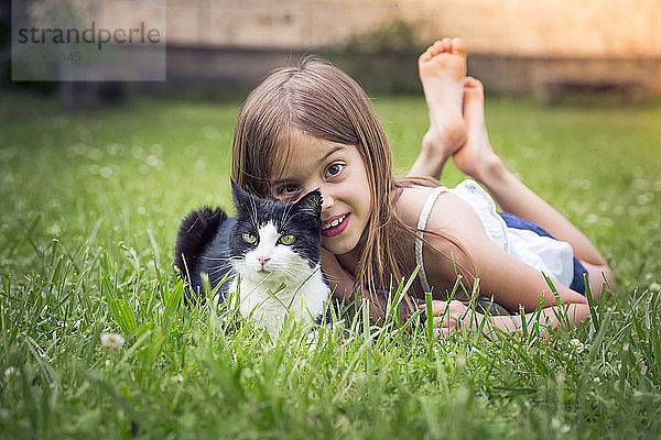 Portrait of little girl with cat lying on a meadow