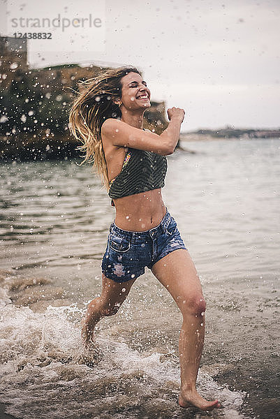 Happy young woman running on the beach splashing with water