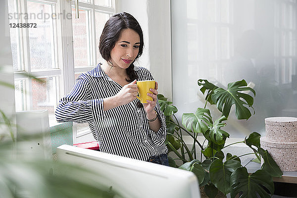 Smiling woman with cup of coffee at the window in office