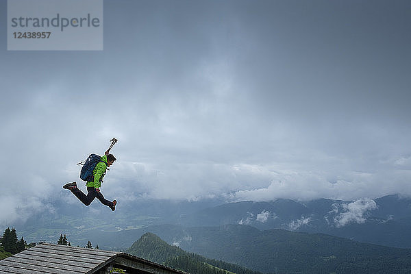 Germany,  Brauneck,  young hiker with hiking poles and backpack jumping in the air