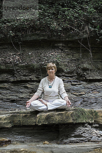 Senior woman doing yoga,  meditating on rock