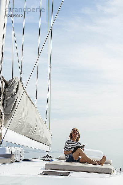 Woman sitting on deck of a catamaran,  reading a book