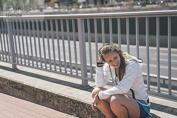 Smiling sportive young woman sitting at motorway