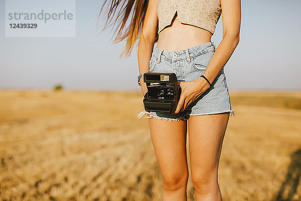 Young woman with instant camera on a field at sunset,  partial view