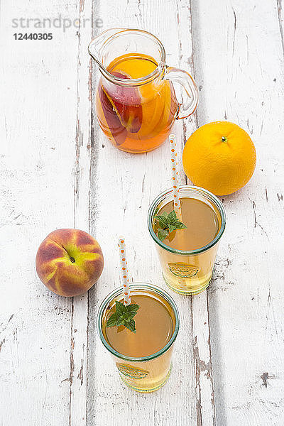 Glasses and jar of peach orange ice tea on wood