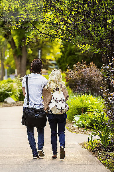 Ein junges Paar geht händchenhaltend einen Weg auf dem Universitätscampus entlang,  Edmonton,  Alberta,  Kanada