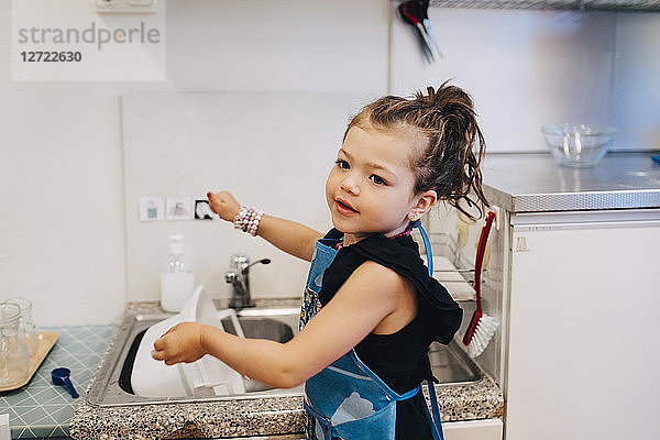 Side view of girl washing utensil in sink at child care
